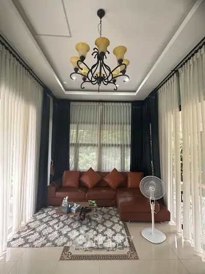 Elegant living room with leather sofa, stylish chandelier, and large windows with curtains.