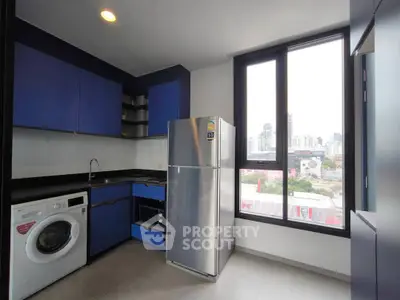 Modern kitchen with blue cabinets, stainless steel fridge, and city view window.