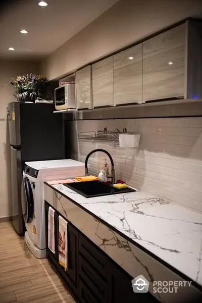 Modern kitchen with marble countertop and washing machine, sleek cabinetry and stylish lighting.