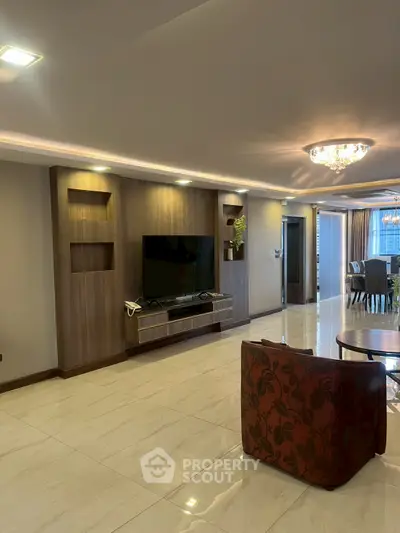Spacious living room with modern decor and elegant lighting, featuring a large TV and stylish furniture.