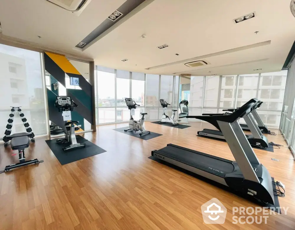 Modern gym with state-of-the-art equipment and large windows in luxury apartment building.