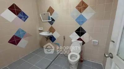 Colorful tiled bathroom with toilet and sink, featuring geometric wall patterns.