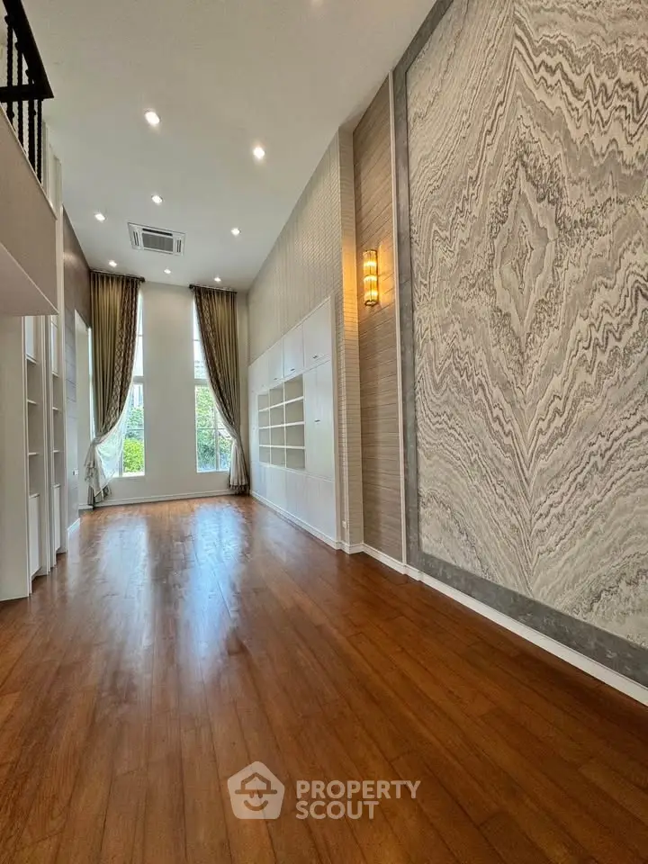 Spacious living room with high ceilings and elegant wall design, featuring large windows and wooden flooring.