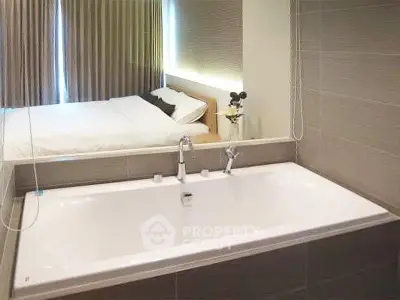 Modern bathroom with bathtub and view into a cozy bedroom, featuring elegant decor and soft lighting.