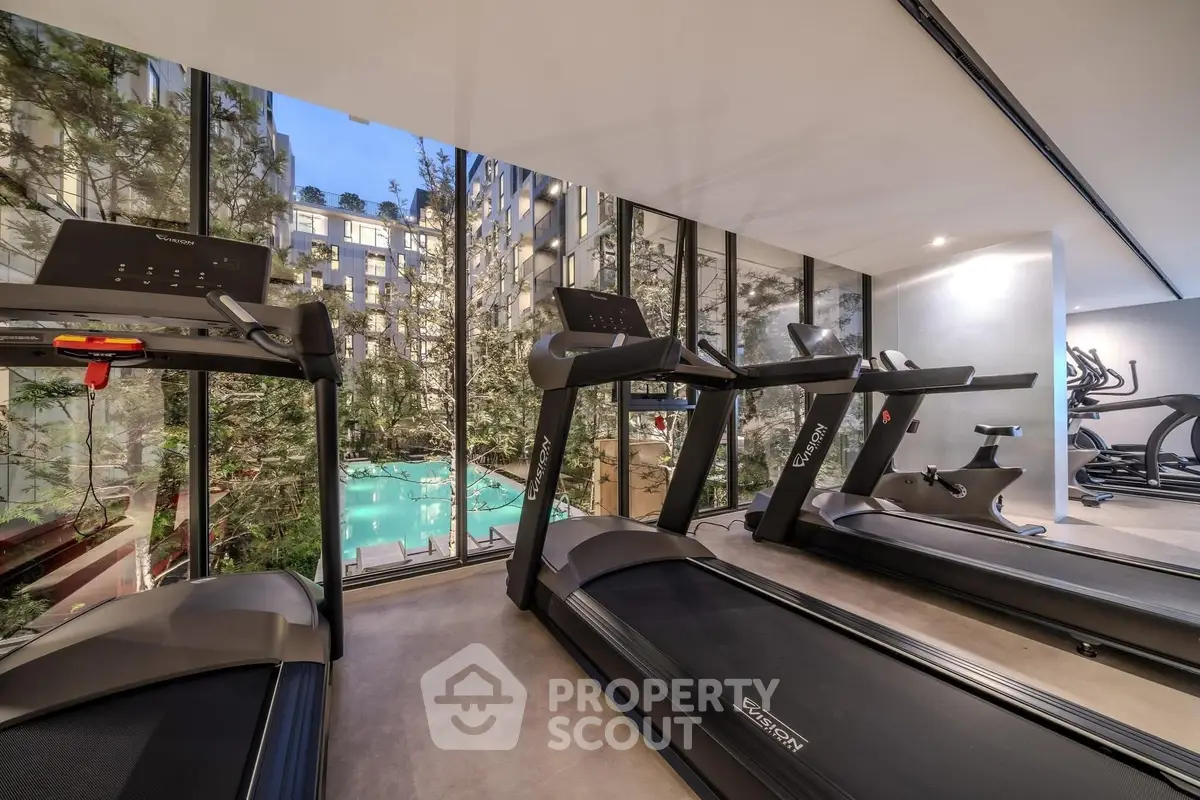 Modern gym with treadmills overlooking a pool and garden view.