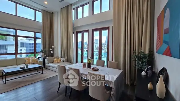 Luxurious living room with high ceilings and elegant dining area, featuring large windows and modern decor.