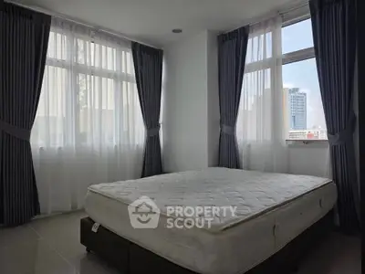 Spacious bedroom with large windows and city view, featuring a comfortable bed and elegant curtains.