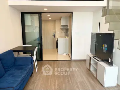 Modern living room with blue sofa, TV, and open kitchen in stylish apartment.