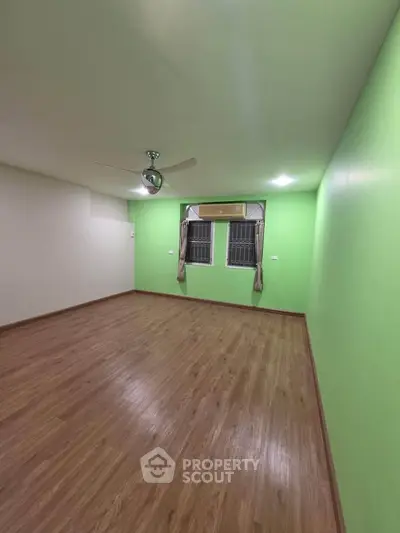 Spacious empty room with wooden flooring and green accent wall, featuring ceiling fan and air conditioning.