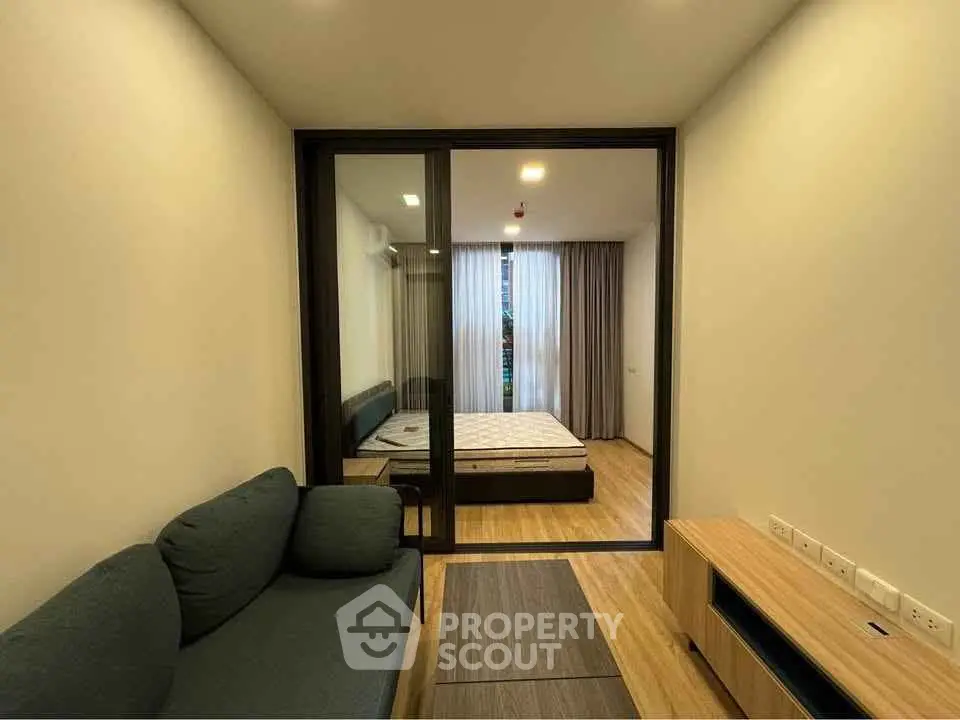 Modern apartment with cozy living room and bedroom separated by glass partition, featuring sleek wooden flooring.