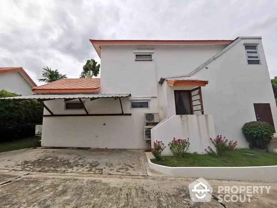 Charming two-story white house with carport and lush garden in serene neighborhood.