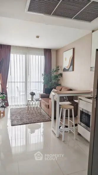 Modern living room with open kitchen, featuring sleek furniture and natural light through large windows.