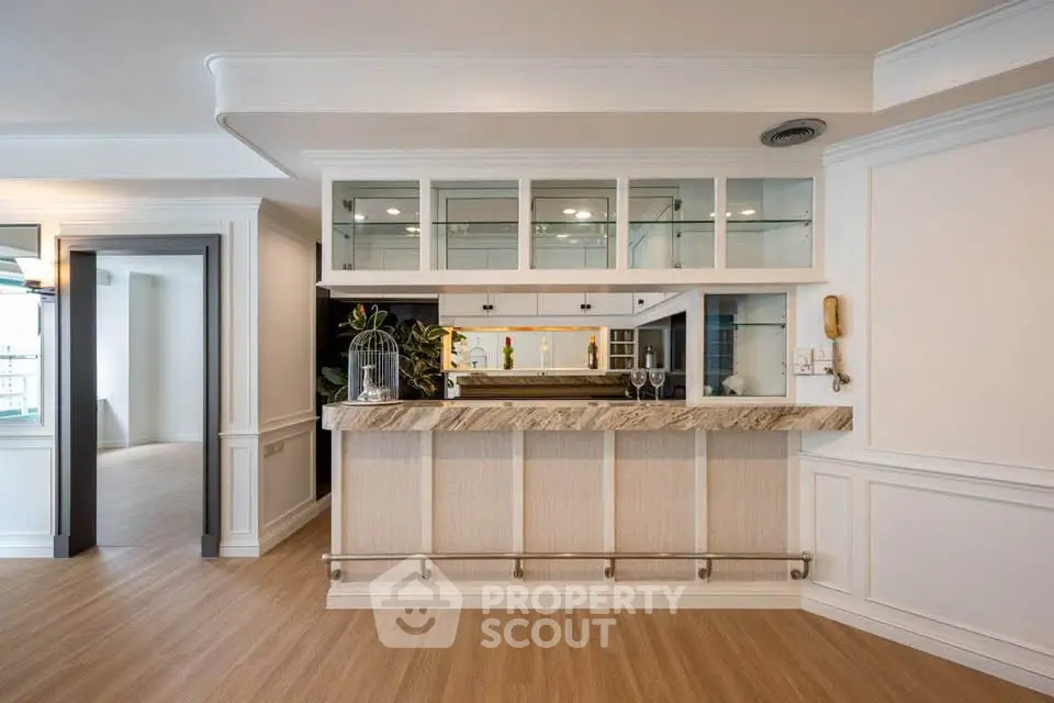 Elegant home bar with marble countertop and glass cabinets in a stylish living space.