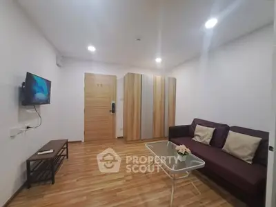 Modern living room with sleek wooden flooring, cozy sofa, and wall-mounted TV in a stylish apartment.