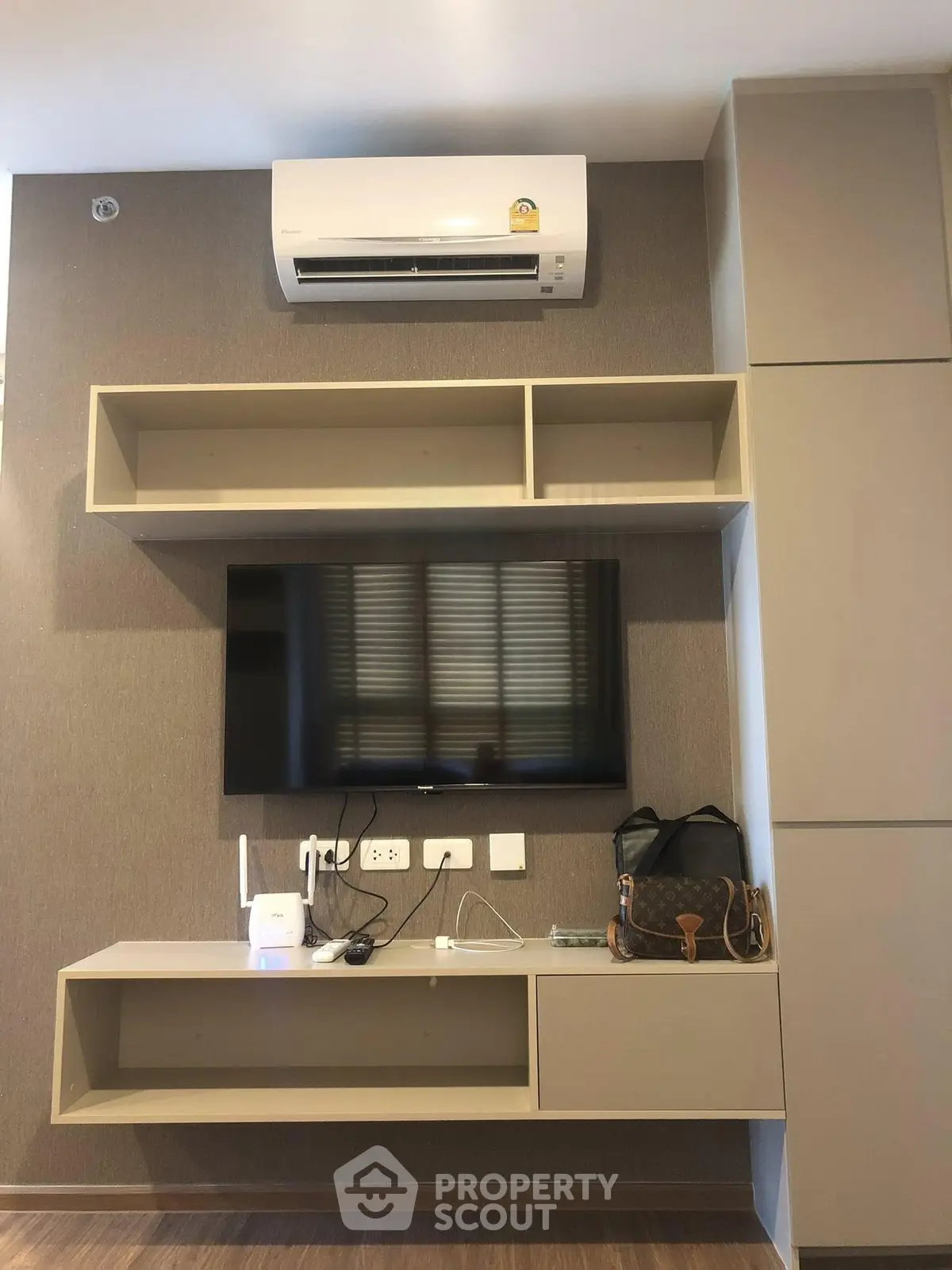 Modern living room with wall-mounted TV and air conditioning unit, featuring sleek storage solutions.