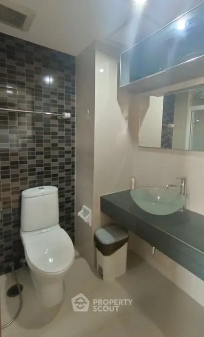 Modern bathroom with sleek design featuring glass sink and stylish tile wall.