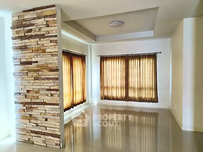 Spacious living room with stone accent wall and large windows with curtains, perfect for natural light.