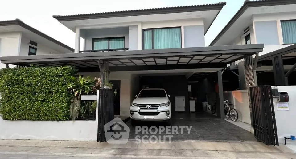 Modern two-story house with carport and lush greenery in a suburban setting.