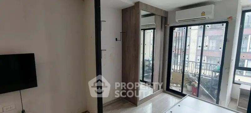 Modern bedroom with large windows and mirrored wardrobe in urban apartment.