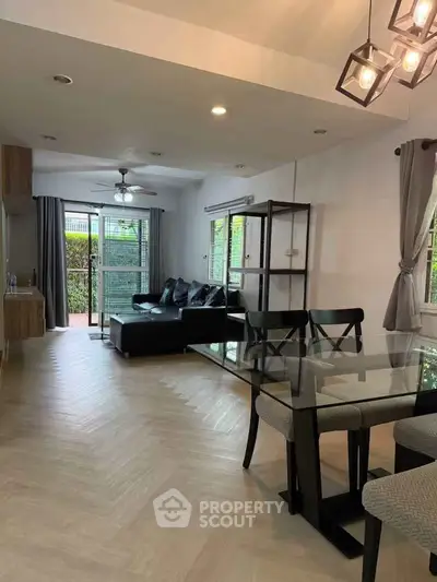 Modern living room with glass dining table and cozy seating area, featuring large windows and stylish lighting.