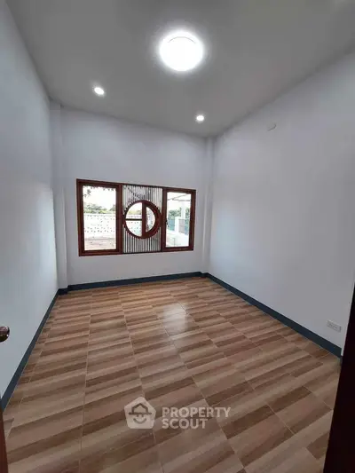 Spacious empty room with wooden flooring and large window, ideal for customization.