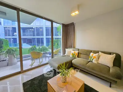 Modern living room with large windows and garden view, featuring stylish green sofa and cozy decor.