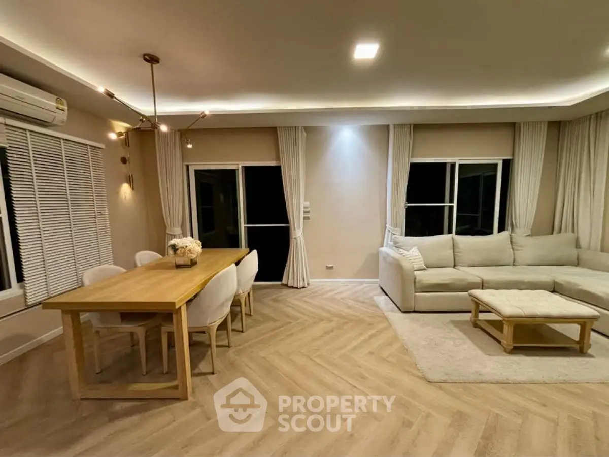 Spacious modern living room with elegant dining area and cozy seating, featuring stylish lighting and large windows.