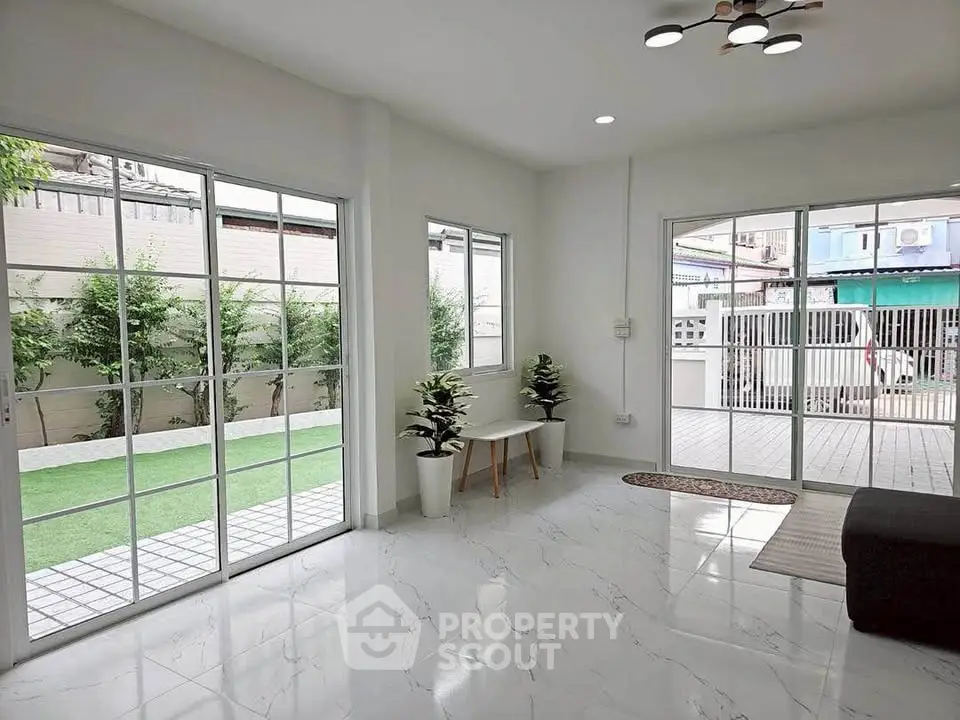 Spacious living room with large windows opening to a private garden, featuring modern flooring and stylish lighting.