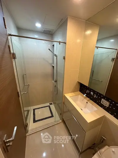 Modern bathroom with glass shower and sleek vanity in contemporary apartment.