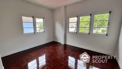 Spacious empty room with polished wooden floors and large windows offering natural light.