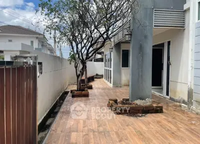 Spacious outdoor patio with wooden flooring and tree, perfect for relaxation.