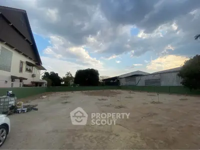 Spacious vacant land with potential for development, surrounded by residential and industrial buildings under a picturesque sky.
