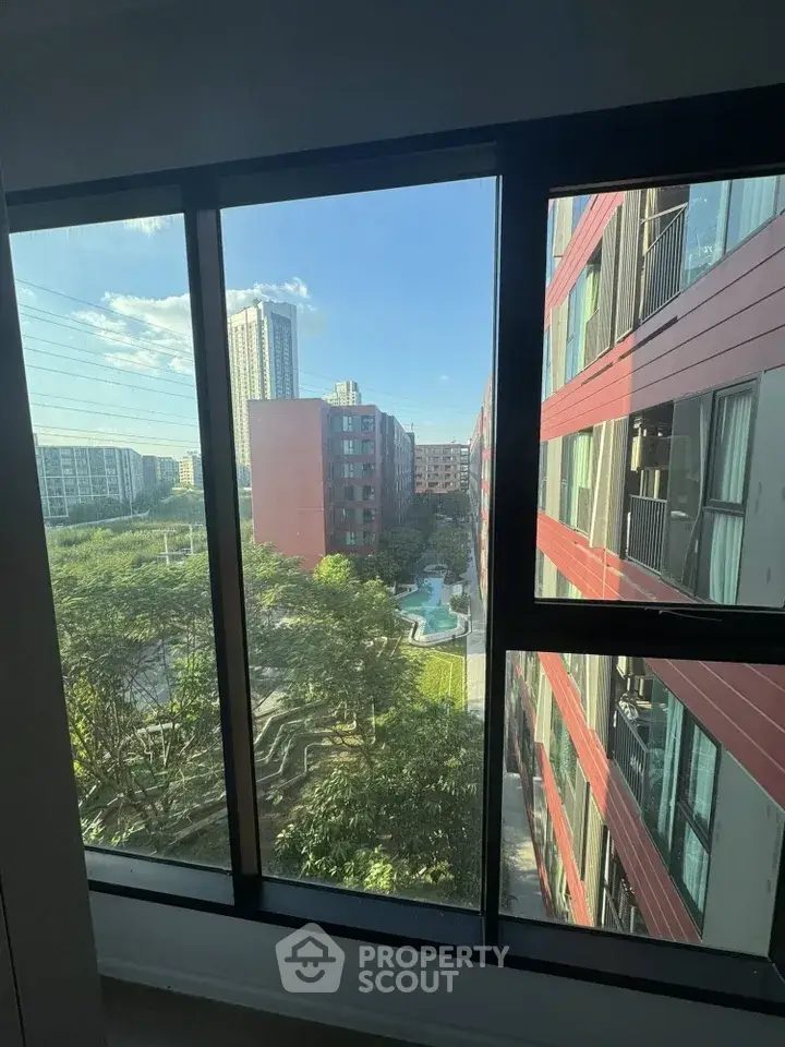 Stunning urban view from high-rise apartment window overlooking modern buildings and lush greenery.