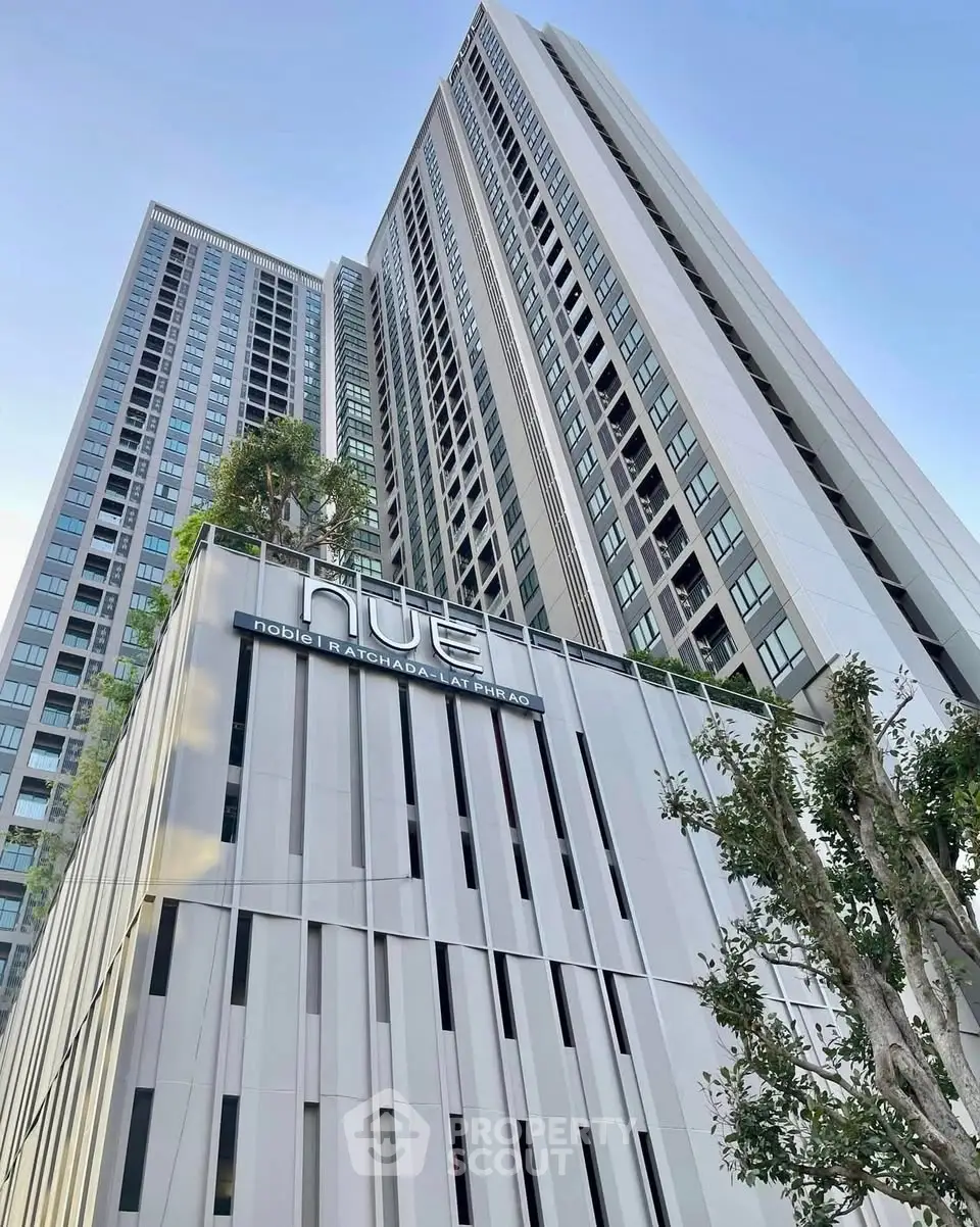 Modern high-rise building with sleek architecture and lush greenery in urban setting.