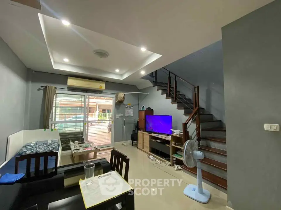 Modern living room with sleek staircase and entertainment center, featuring stylish lighting and cozy seating area.