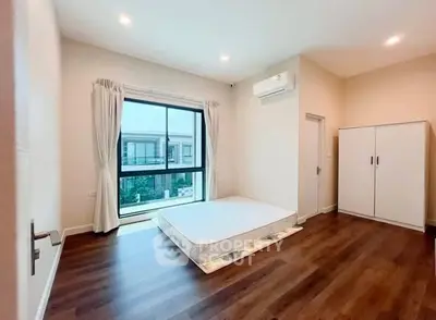 Spacious bedroom with large window and wooden flooring in modern apartment.