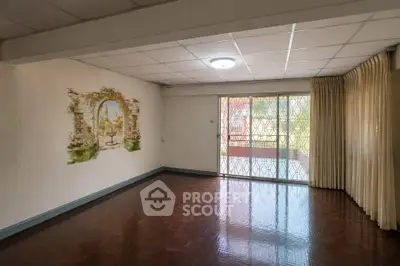 Spacious living room with parquet flooring and decorative wall art, featuring large windows for natural light.