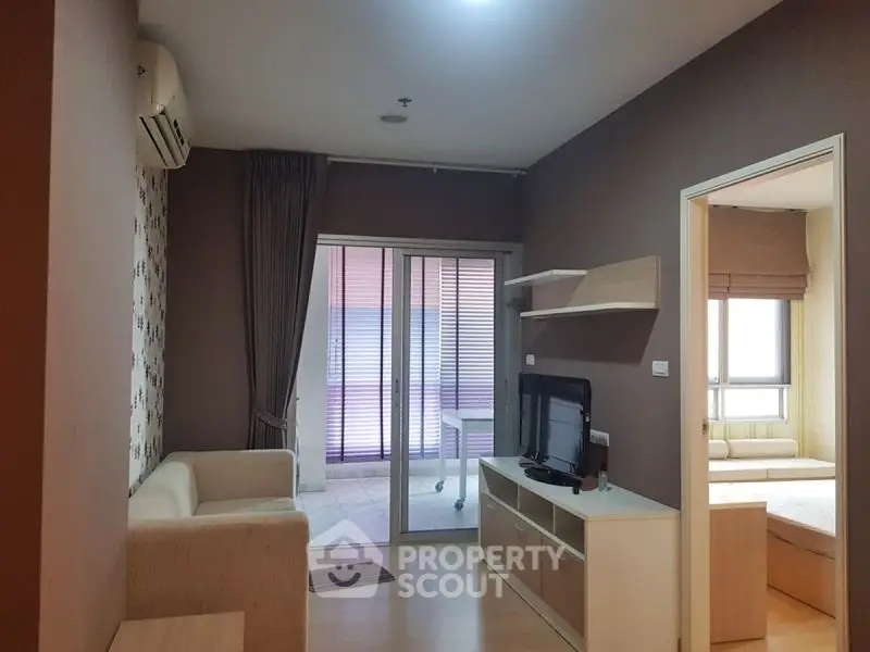 Modern living room with cozy sofa and TV unit, leading to a bright balcony area.