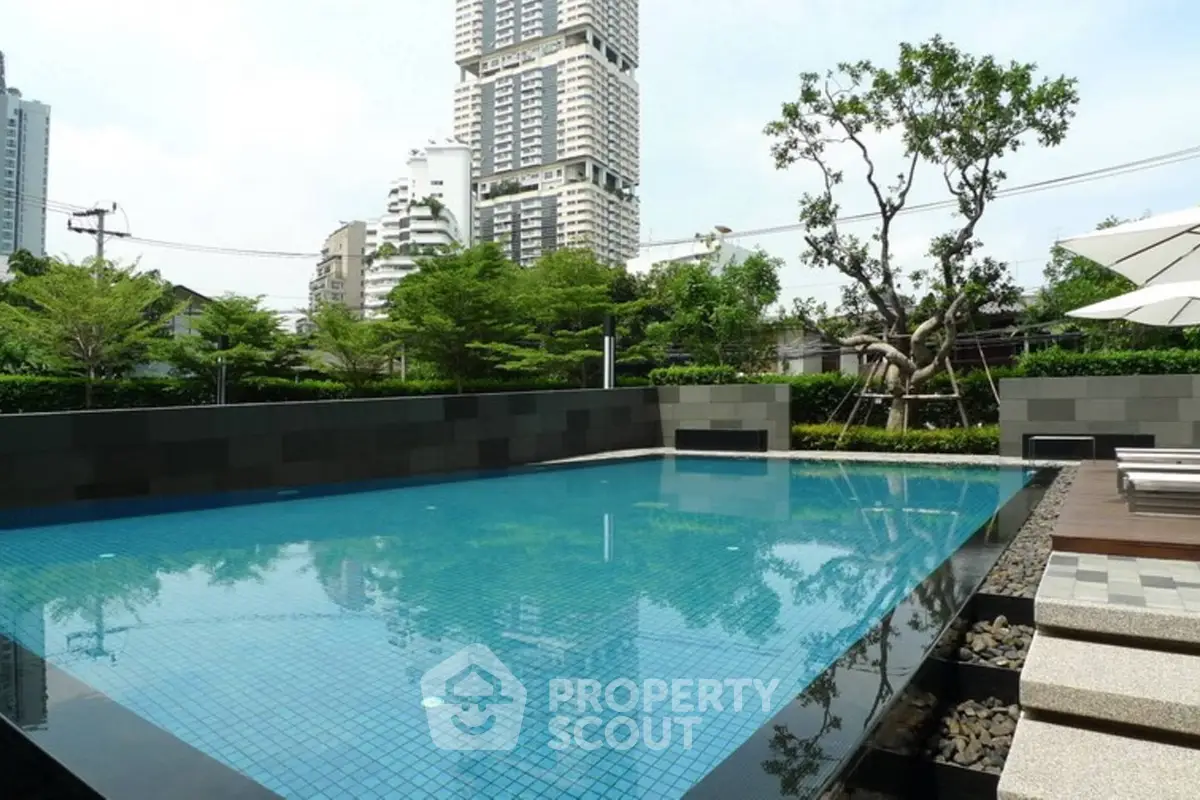 Luxurious urban swimming pool with cityscape view and lush greenery.