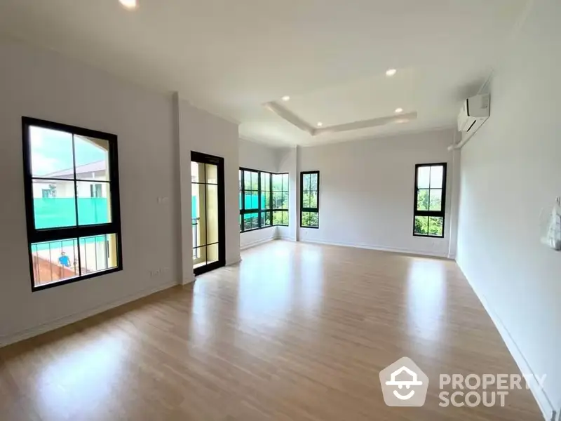 Spacious and bright living area with gleaming hardwood floors, multiple windows offering ample natural light, and a versatile open floor plan perfect for modern living.