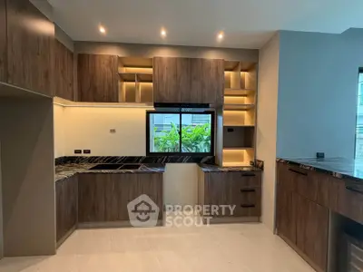 Modern kitchen with sleek wooden cabinets and marble countertops, featuring an open layout and large window view.