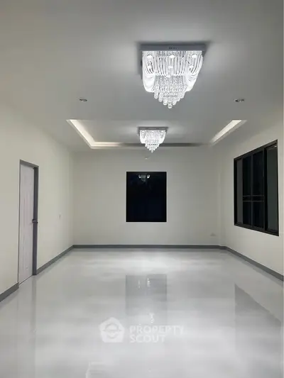 Spacious modern living room with elegant chandeliers and glossy white flooring.