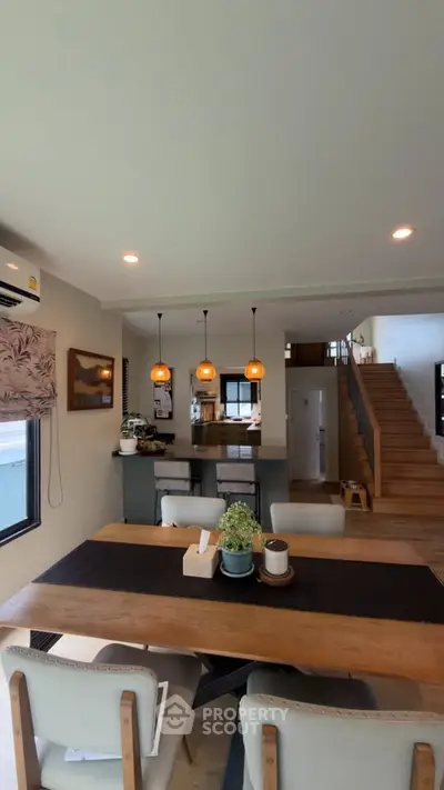 Modern open-plan living and dining area with stylish lighting and wooden staircase.
