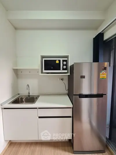 Modern compact kitchen with stainless steel fridge and microwave, perfect for urban living.