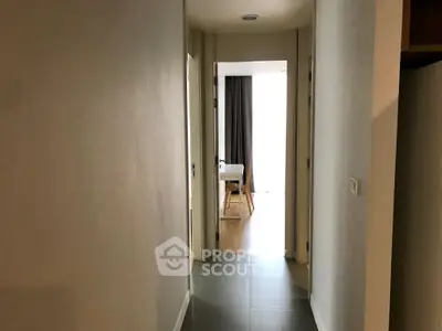 Modern apartment hallway leading to a bright room with wooden flooring and curtains.
