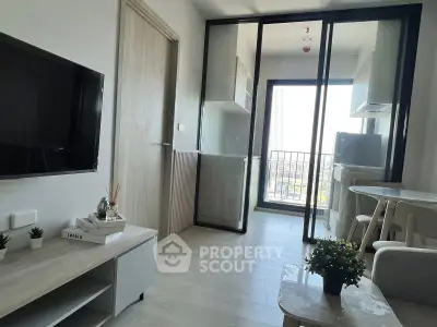 Modern living room with open kitchen and balcony view, featuring sleek furniture and natural light.