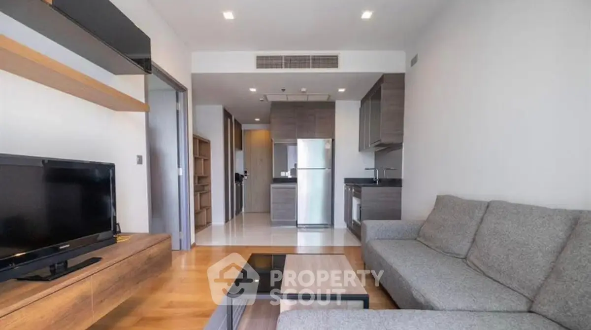 Modern living room with open kitchen, sleek furniture, and wooden flooring in a stylish apartment.