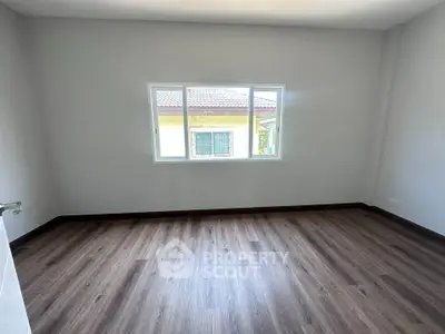 Spacious empty room with wooden flooring and large window, perfect for customization.