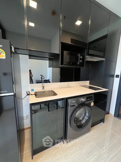 Modern kitchen with sleek black cabinetry and built-in appliances, featuring a washing machine and induction cooktop.