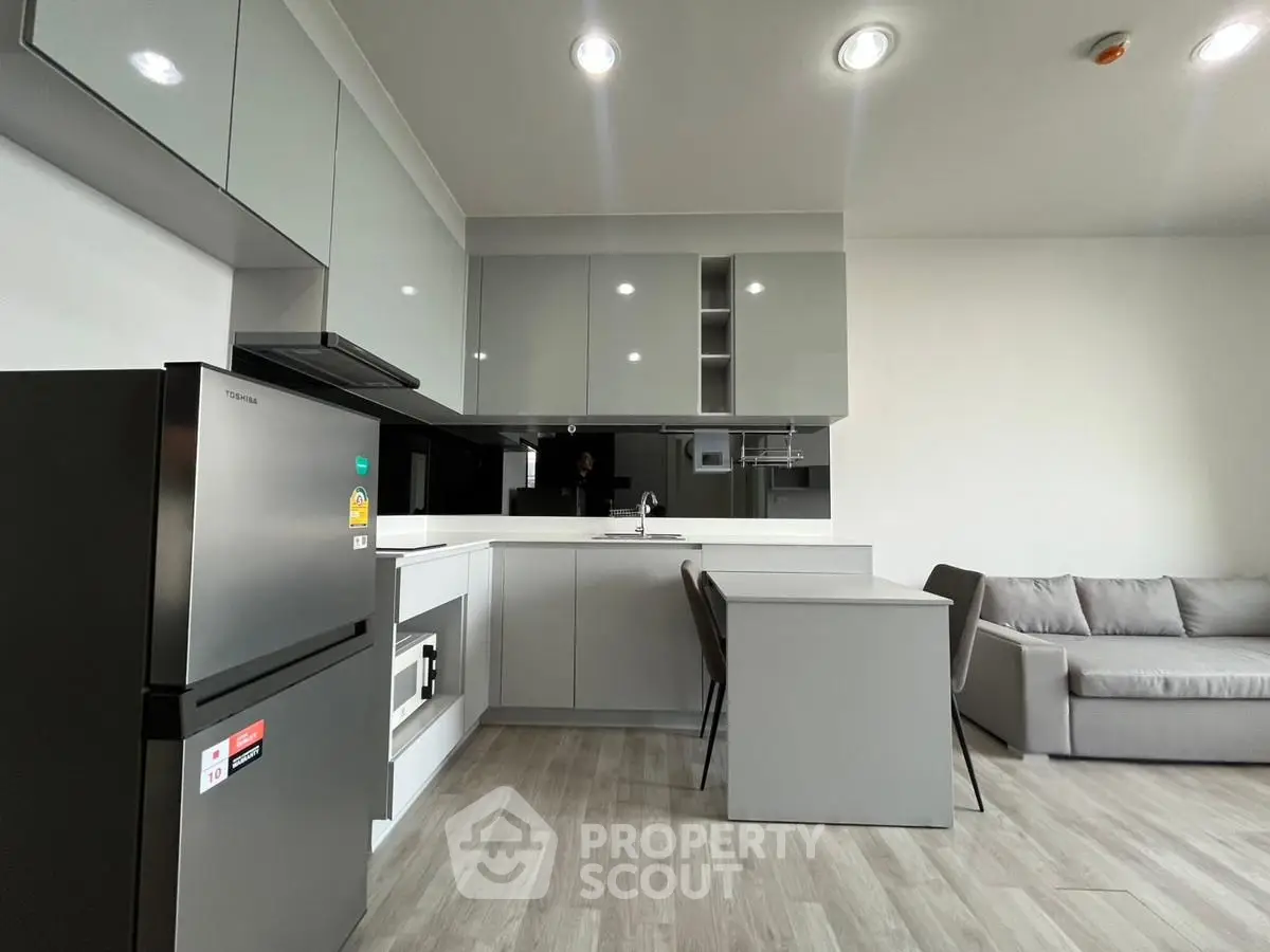Modern kitchen with sleek cabinetry and cozy living area in open layout apartment.